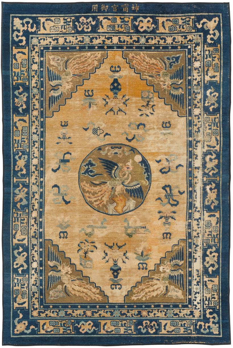 La figura mostra un grande tappeto in cui prevalgono i colori blu e giallo; quest’ultimo realizzato con fili di seta ricoperti da lamine metalliche.