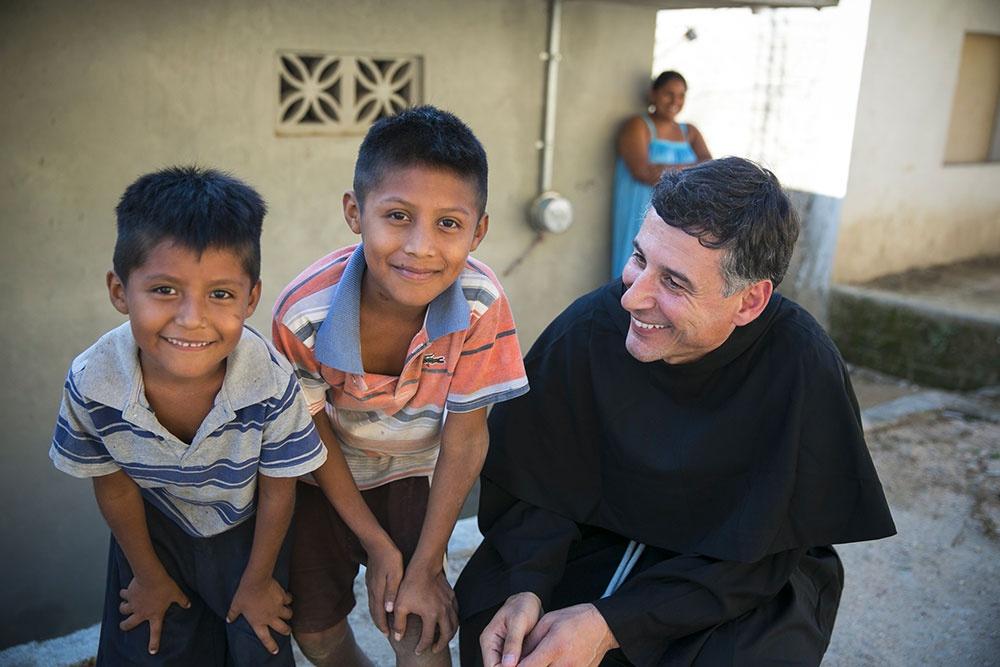 Padre Fortunato in compagnia di due bambini sorridenti che guardano l’obiettivo.
