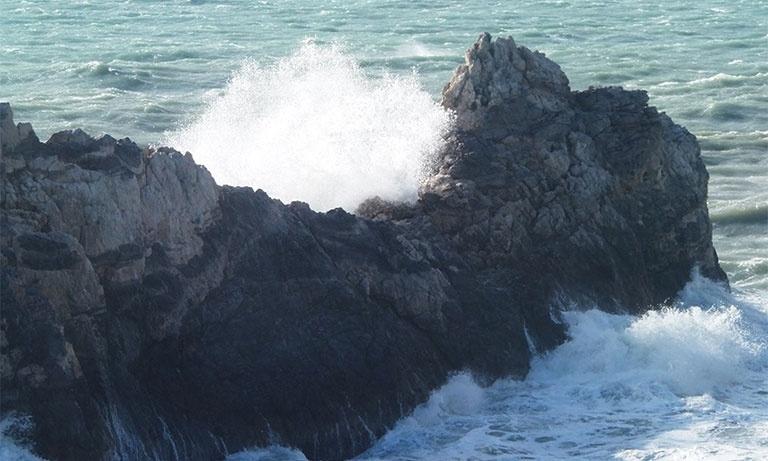 Immagine del mare che si infrange sugli scogli e si trasforma in un’onda spumeggiante. 